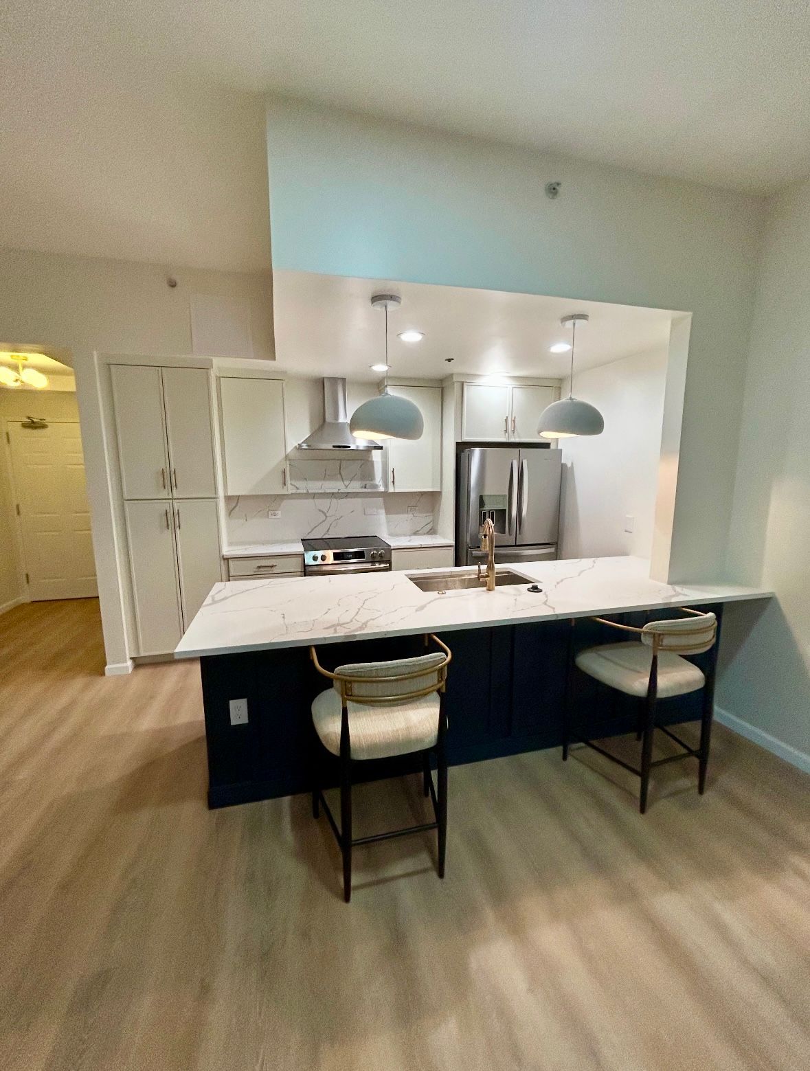 Modern kitchen with navy blue island, white countertops, stainless steel appliances, and two bar stools.
