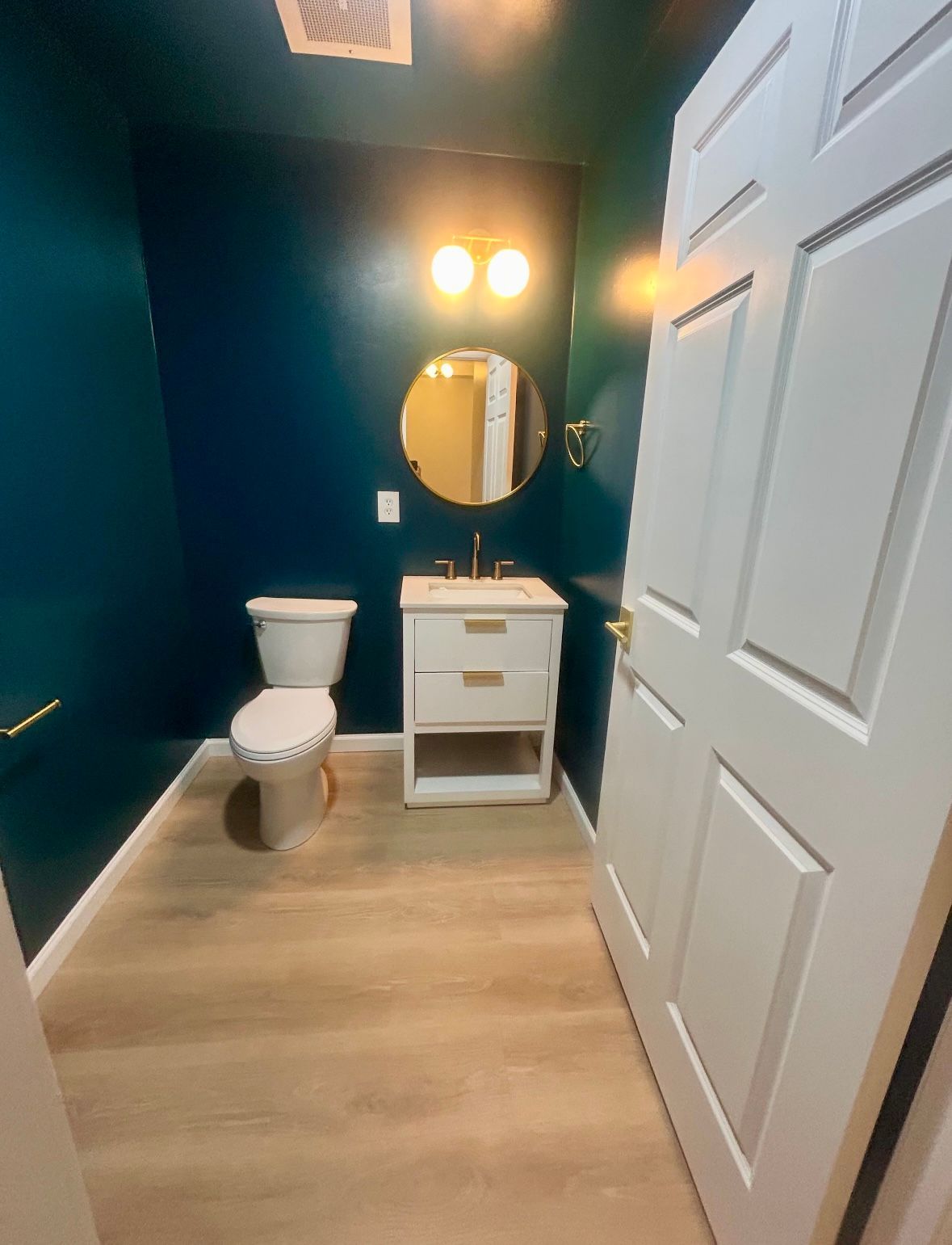 Small bathroom with blue walls, white fixtures, and light wood-look flooring.