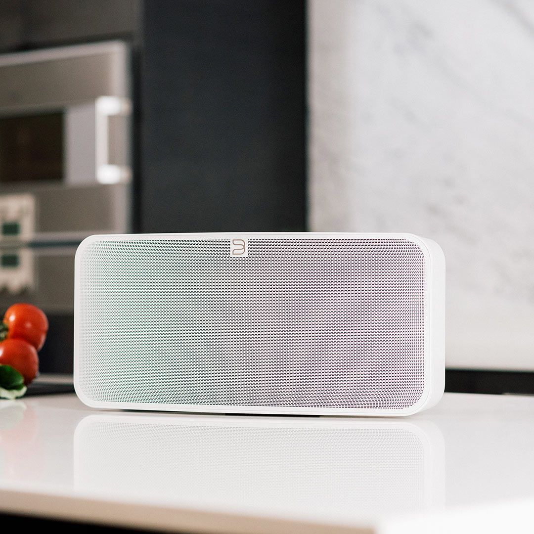 A white speaker is sitting on a counter in a kitchen.