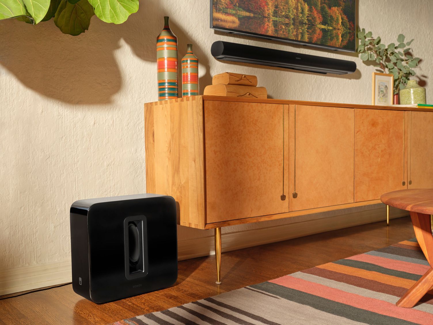 A living room with a wooden cabinet , a striped rug , a subwoofer , and a television.