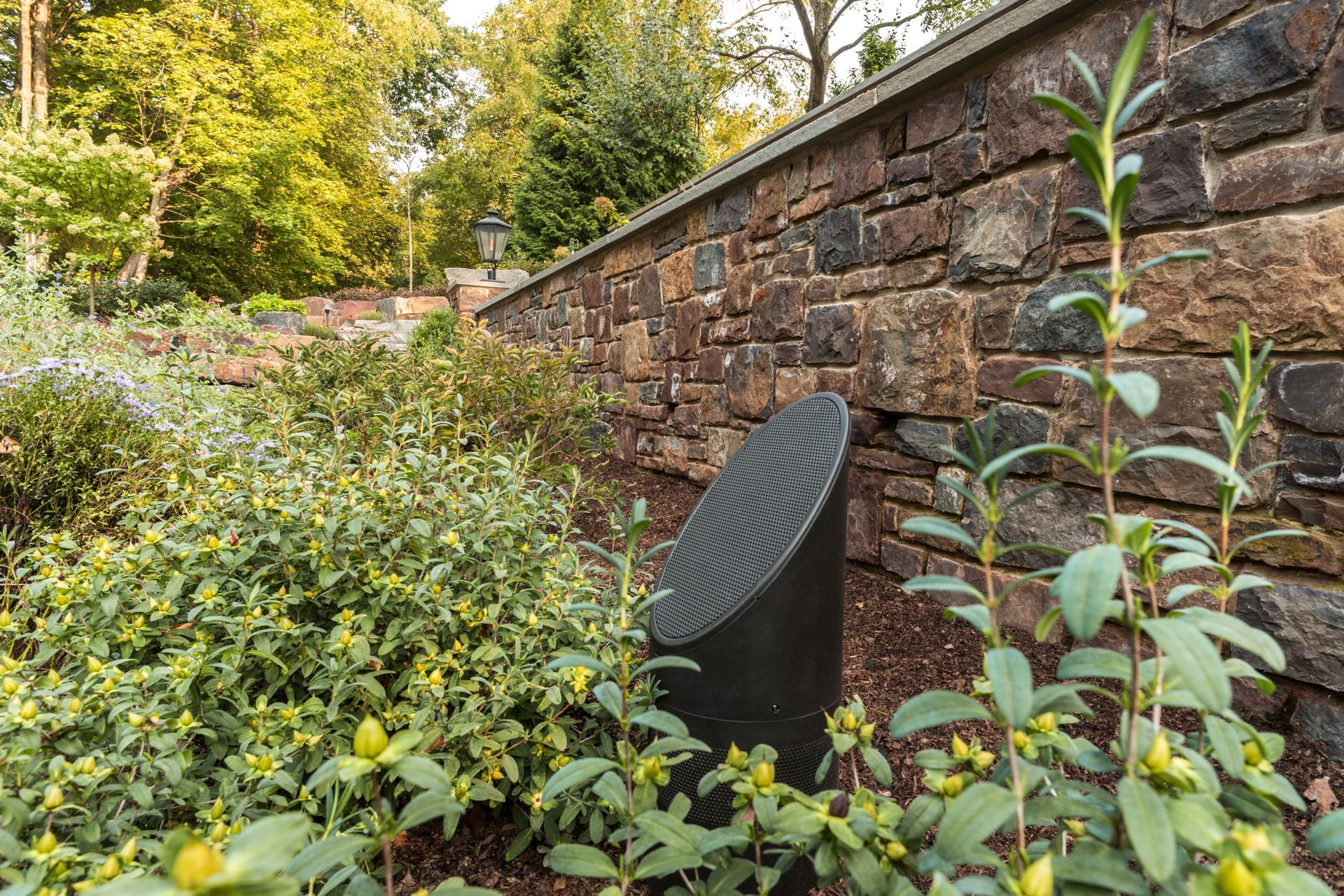 A speaker is sitting in the middle of a garden next to a stone wall.