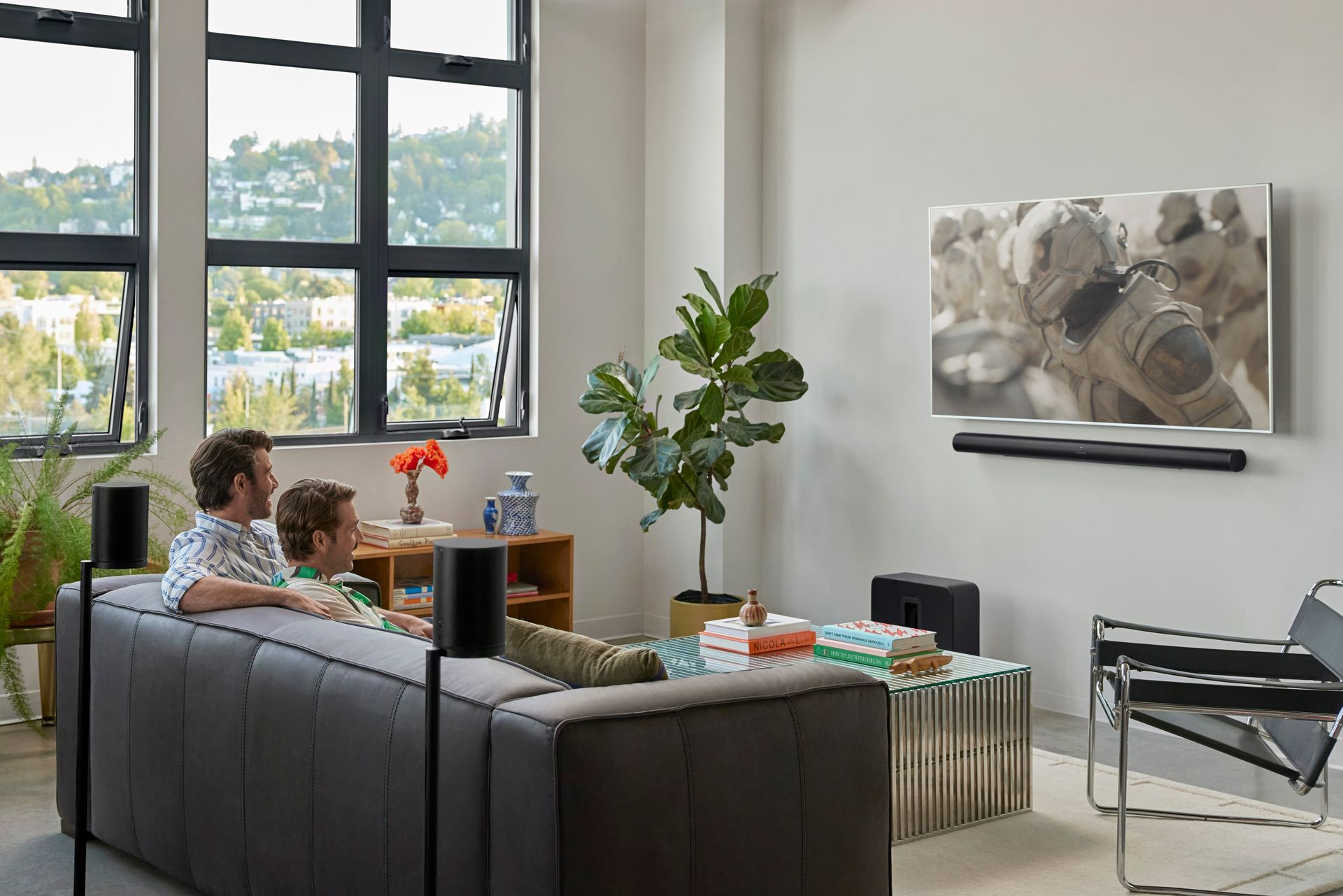Two people are sitting on a couch in a living room watching a television.