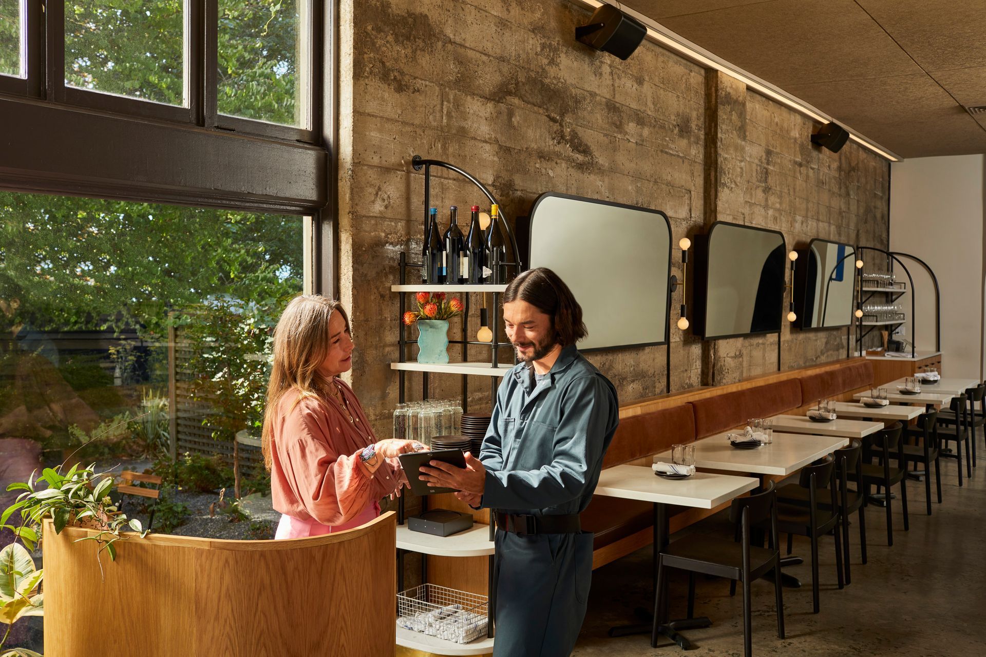 A man and a woman are standing in a restaurant looking at a tablet.