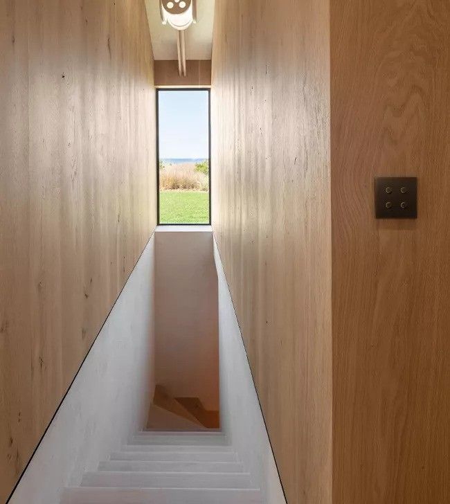 A narrow hallway with wooden walls and stairs leading up to a window