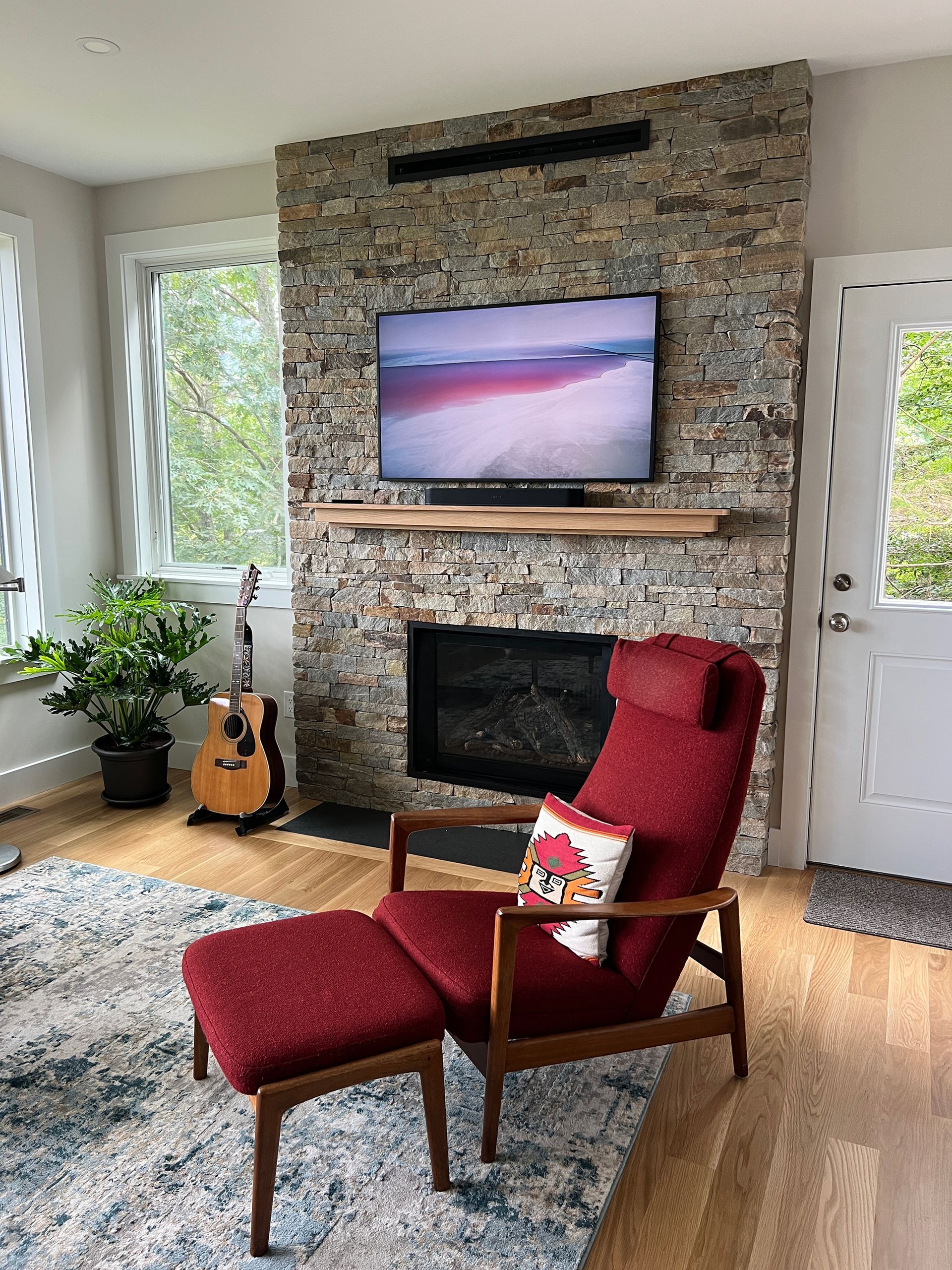 A living room with a fireplace, chair, ottoman, and television.