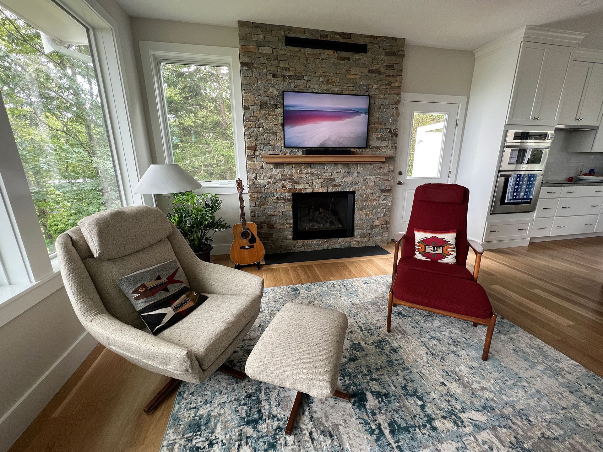 A living room with two chairs, an ottoman, a fireplace ,and a television.