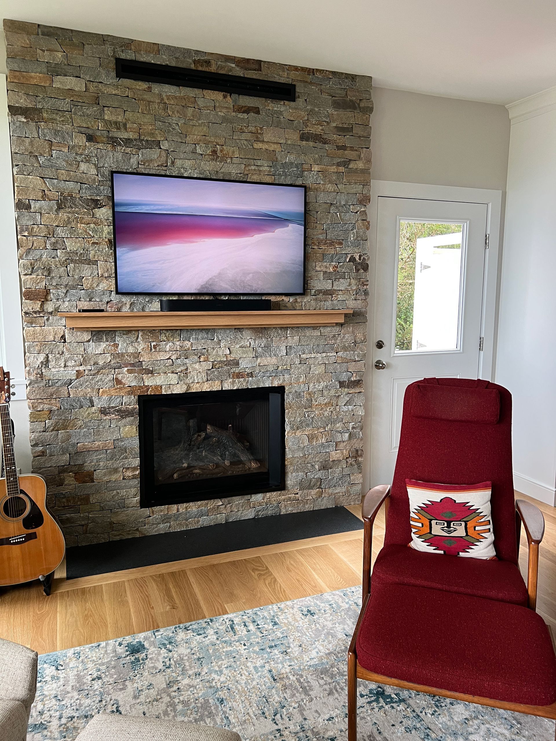 A living room with a fireplace, television, chair ,and guitar.
