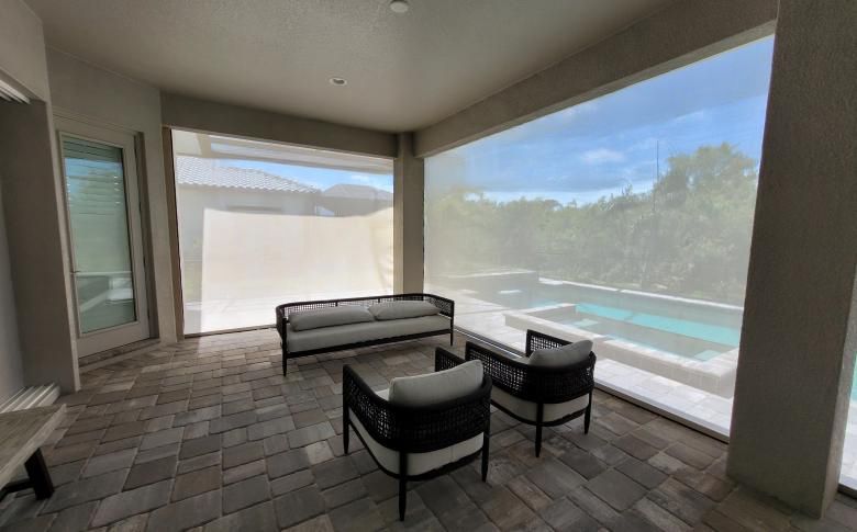 A patio with a couch and chairs and a swimming pool in the background