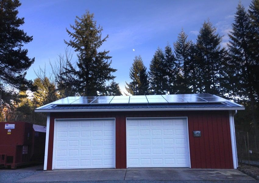 a red garage with two white garage doors and solar panels on the roof