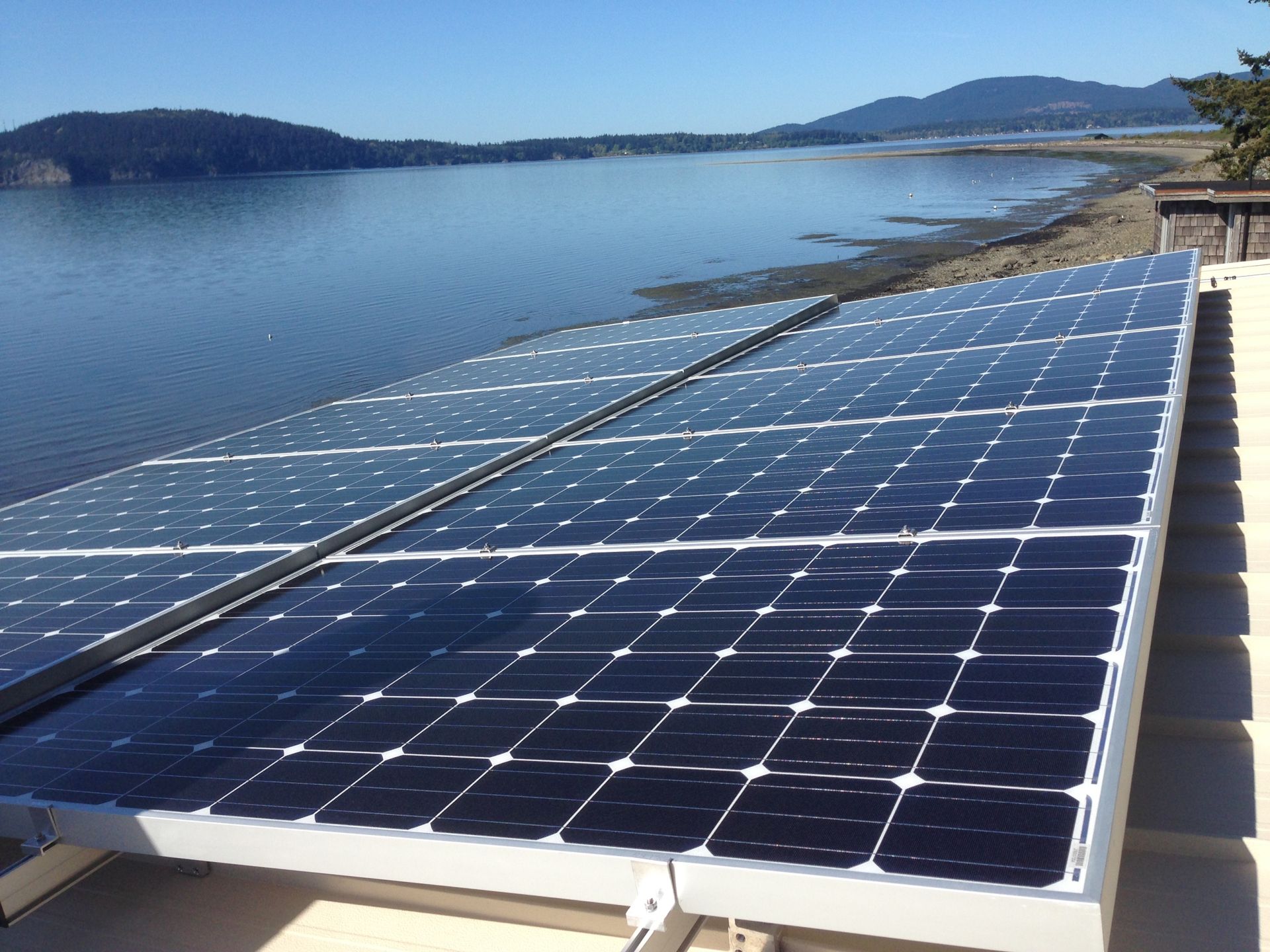 a row of solar panels sitting on top of a roof next to a body of water