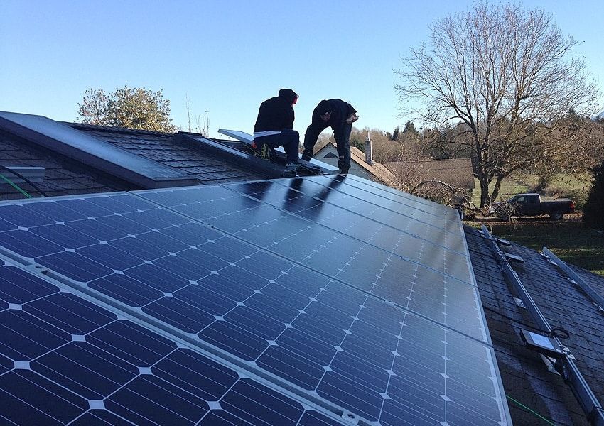 two men are installing solar panels on the roof of a house