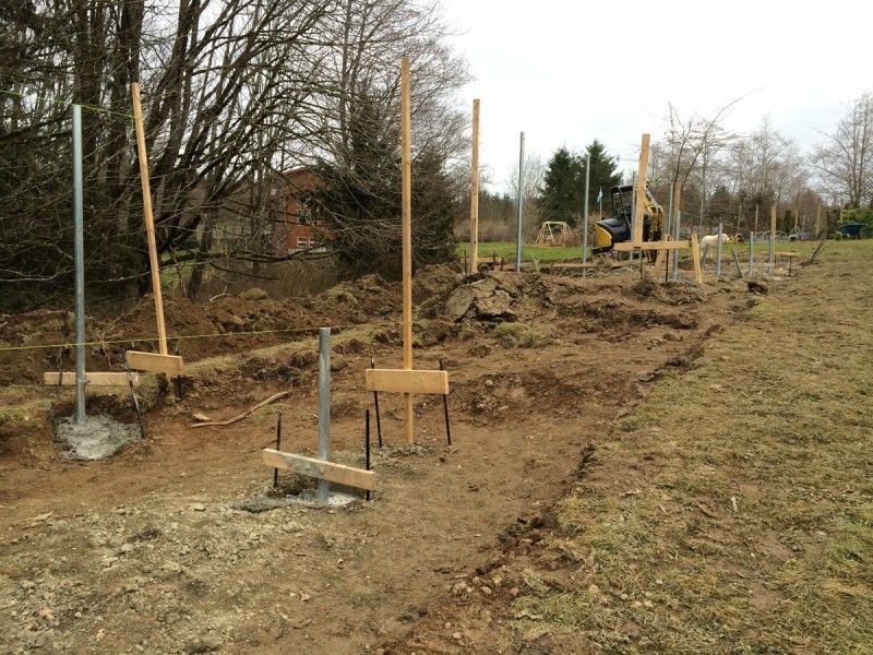a row of wooden posts in a dirt field with trees in the background