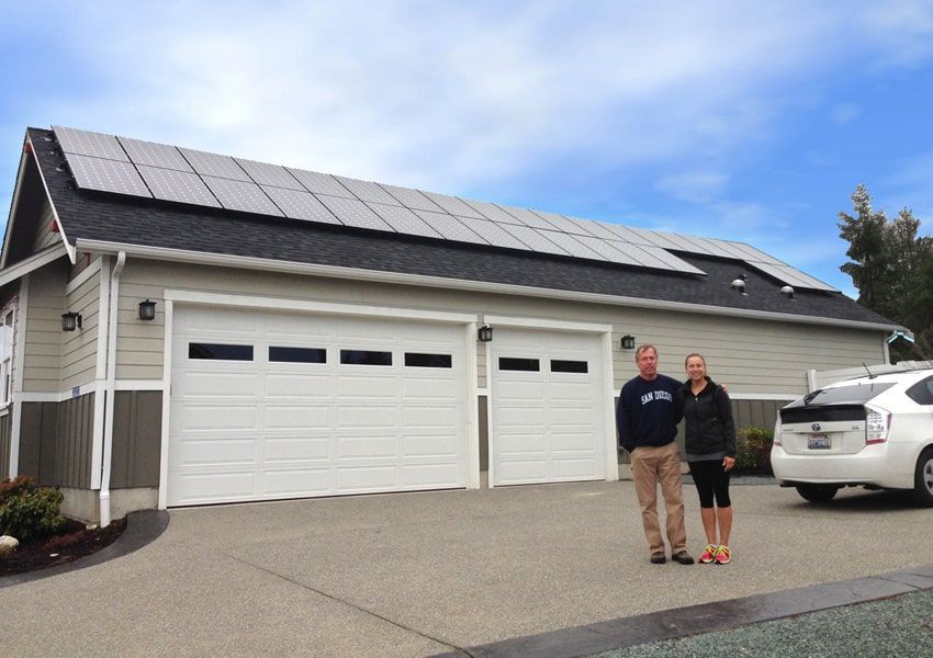 a man and a woman are standing in front of a garage with solar panels on the roof