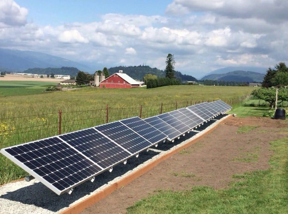 a row of solar panels in a field with a red barn in the background