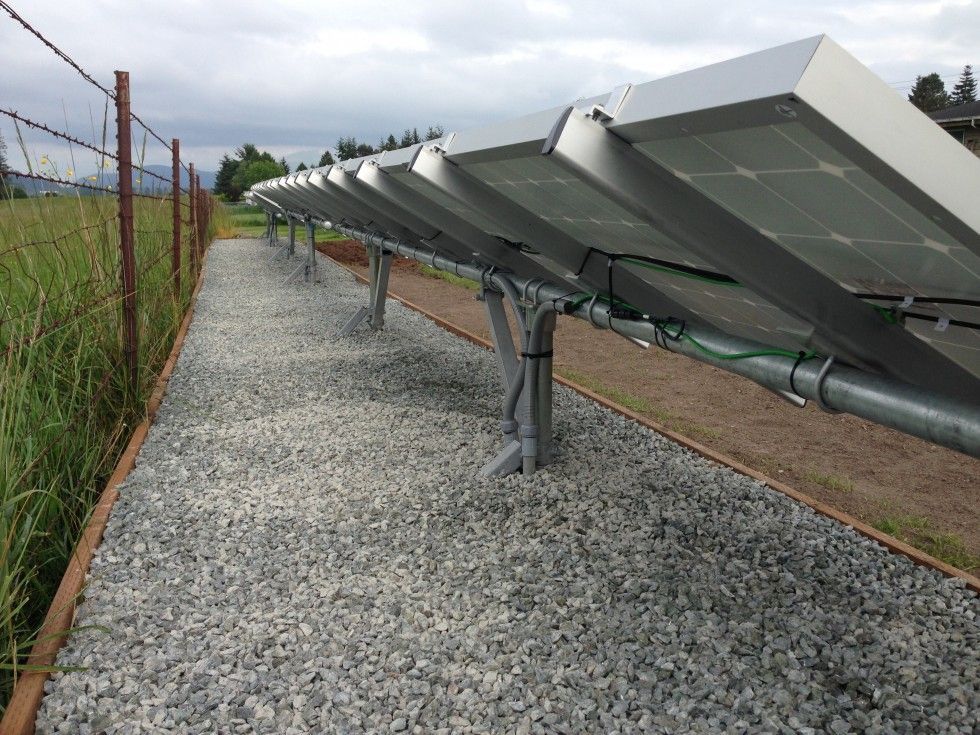 a row of solar panels sitting on top of gravel next to a fence