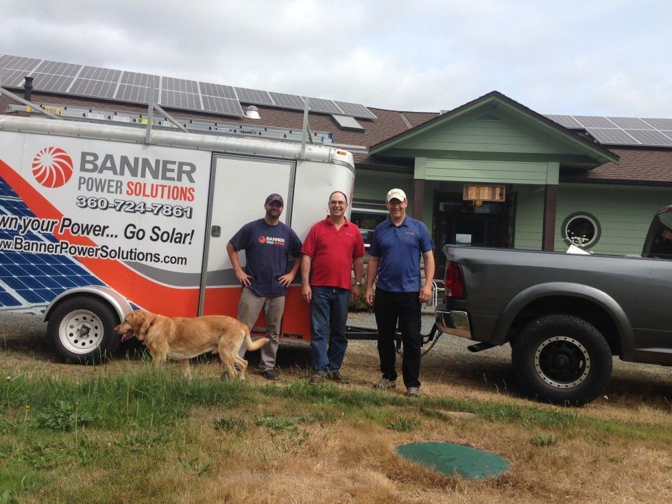 three men and a dog are standing in front of a banner power solutions van