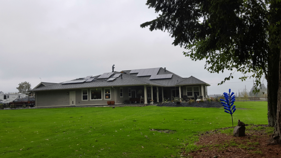 a large house with solar panels on the roof is sitting on top of a lush green field