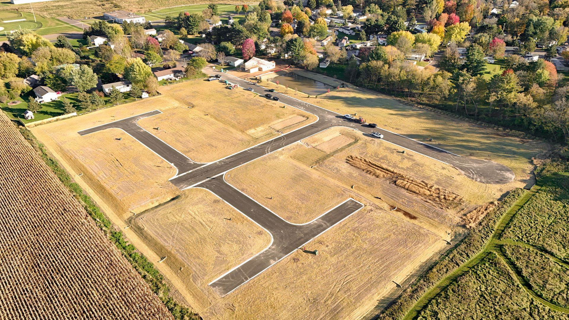 Aerial view of a cleared residential development site with paved roads and undeveloped lots. Brown fields, autumn trees.