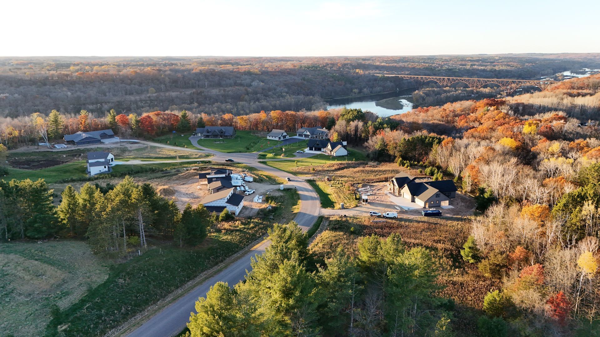 Aerial view of houses and road in a rural area with autumn foliage and a river in the distance.