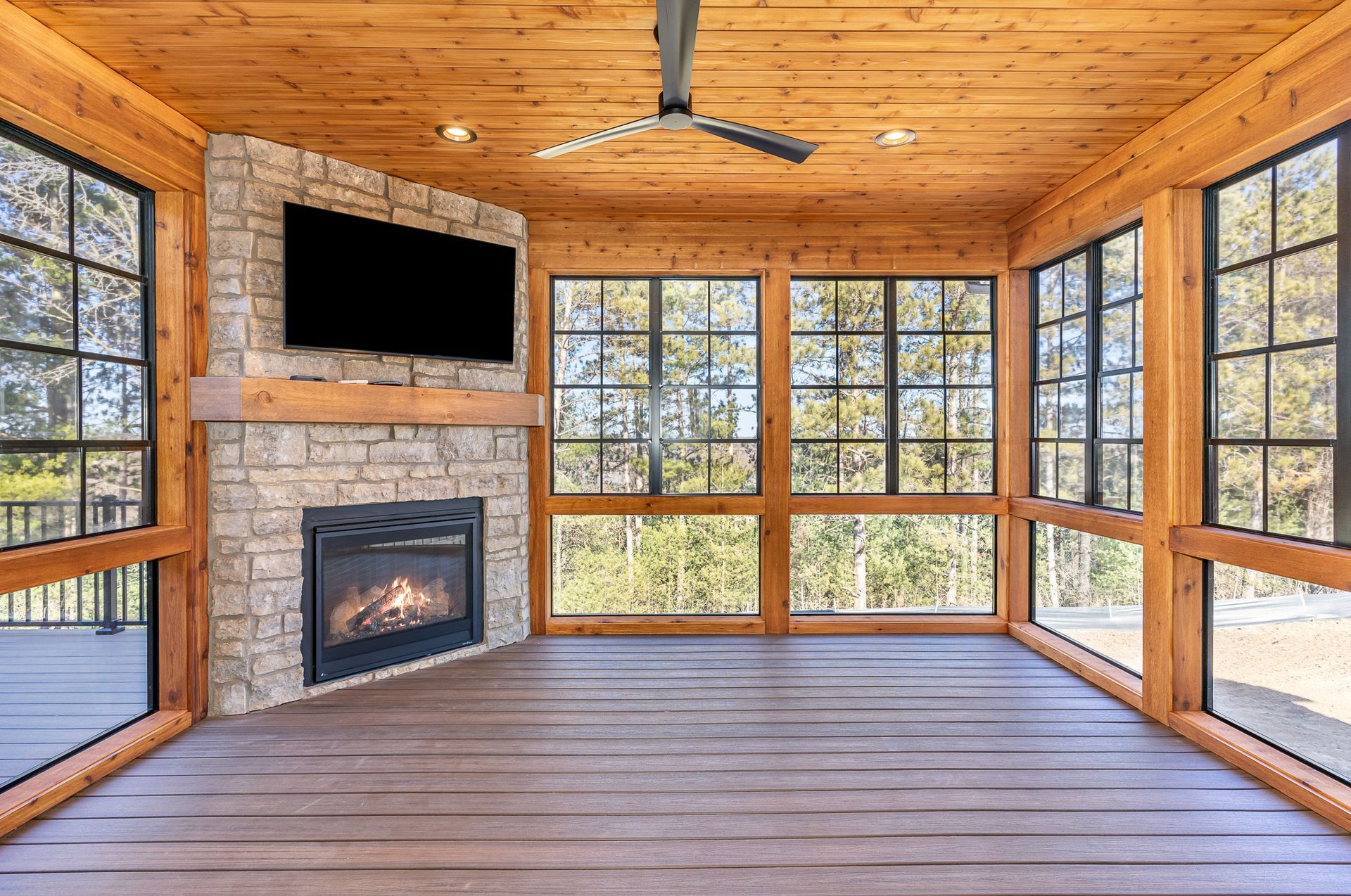 A screened in porch with a fireplace and a flat screen tv.