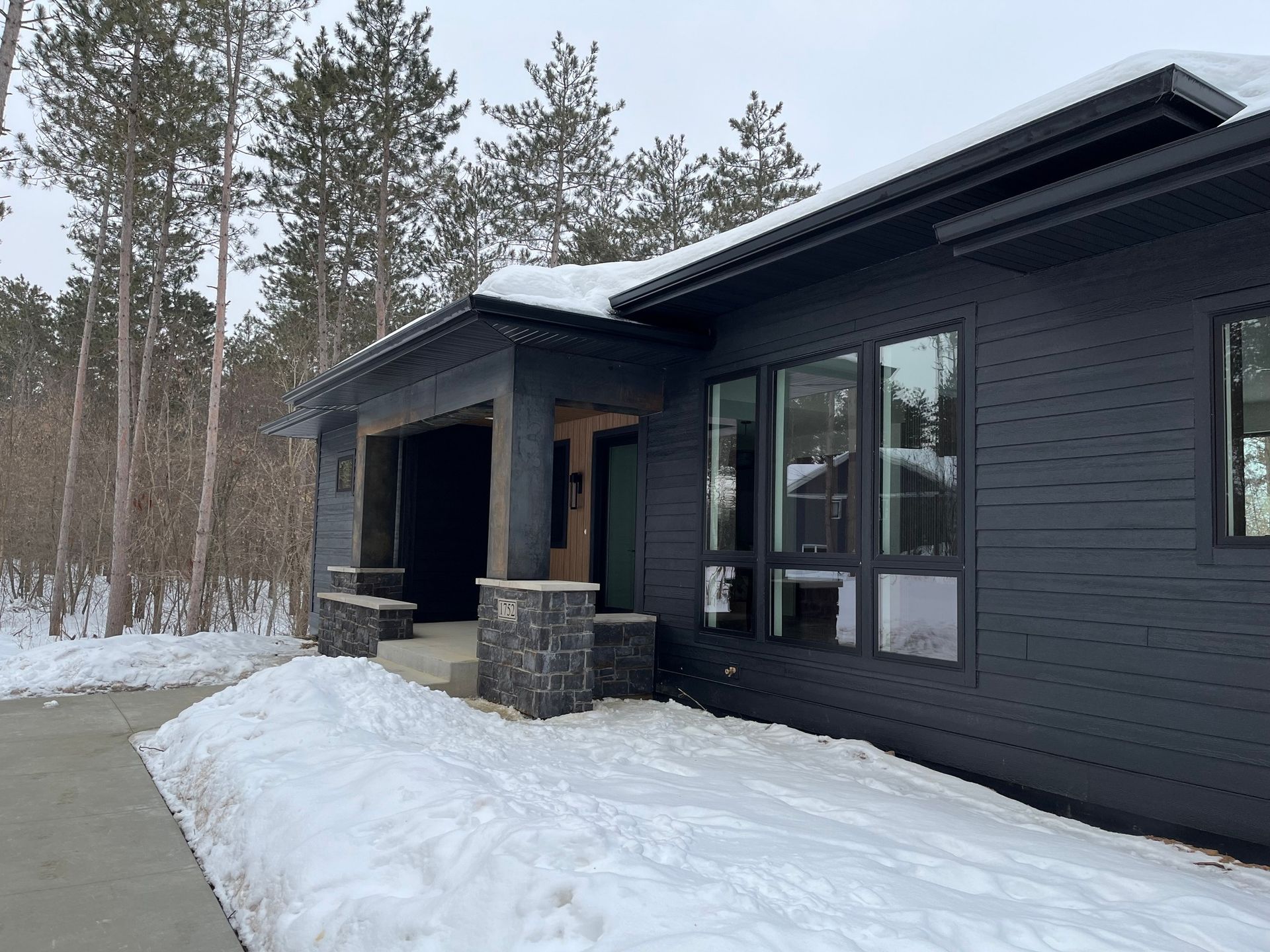 A black house with snow on the ground and trees in the background.