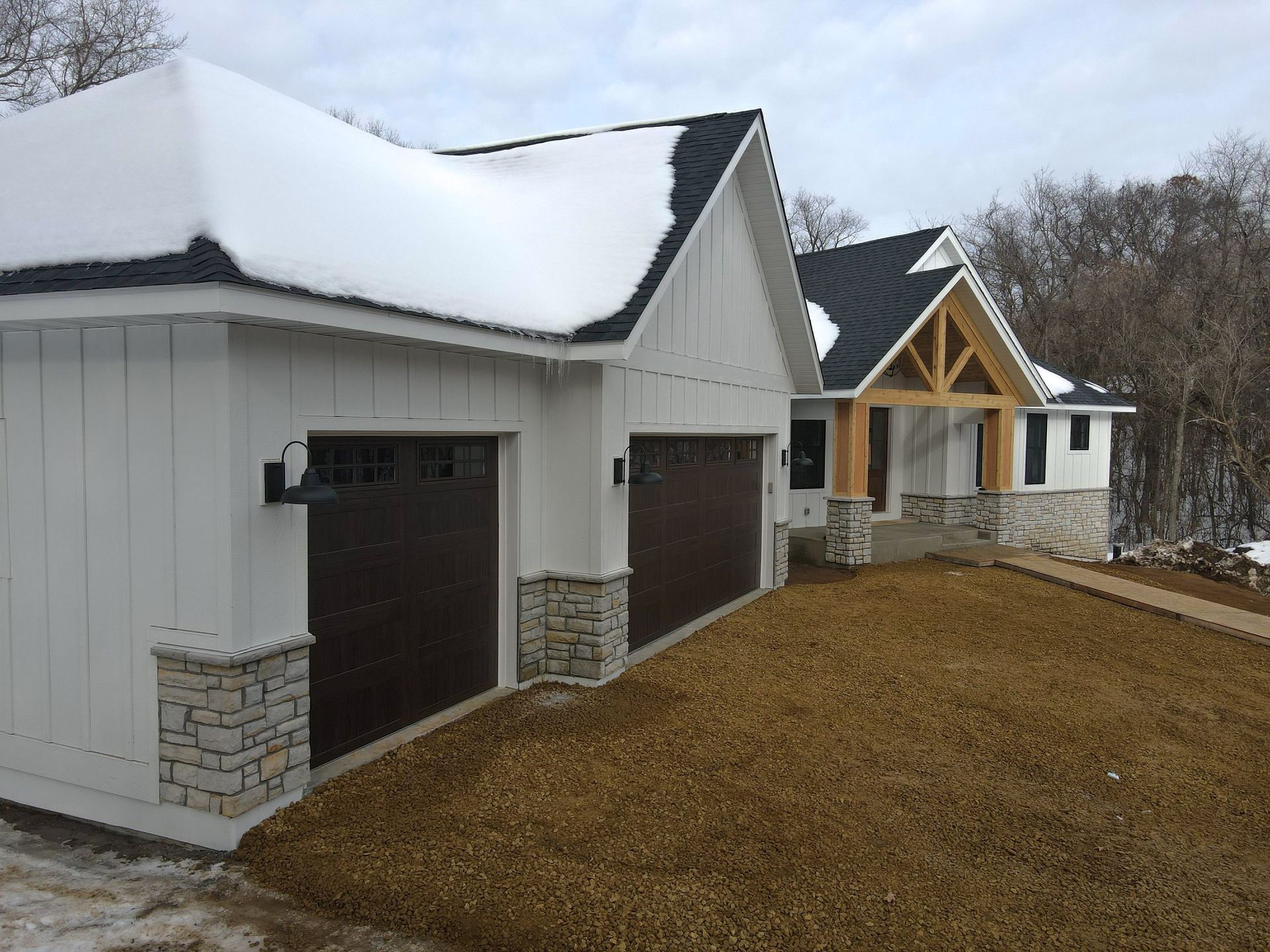 A white house with two garage doors and a snowy roof