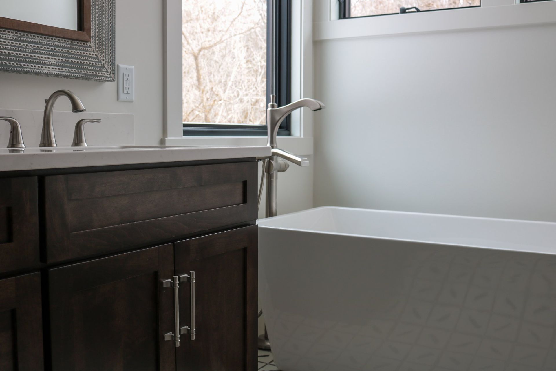 A bathroom with a tub, sink, mirror and window.