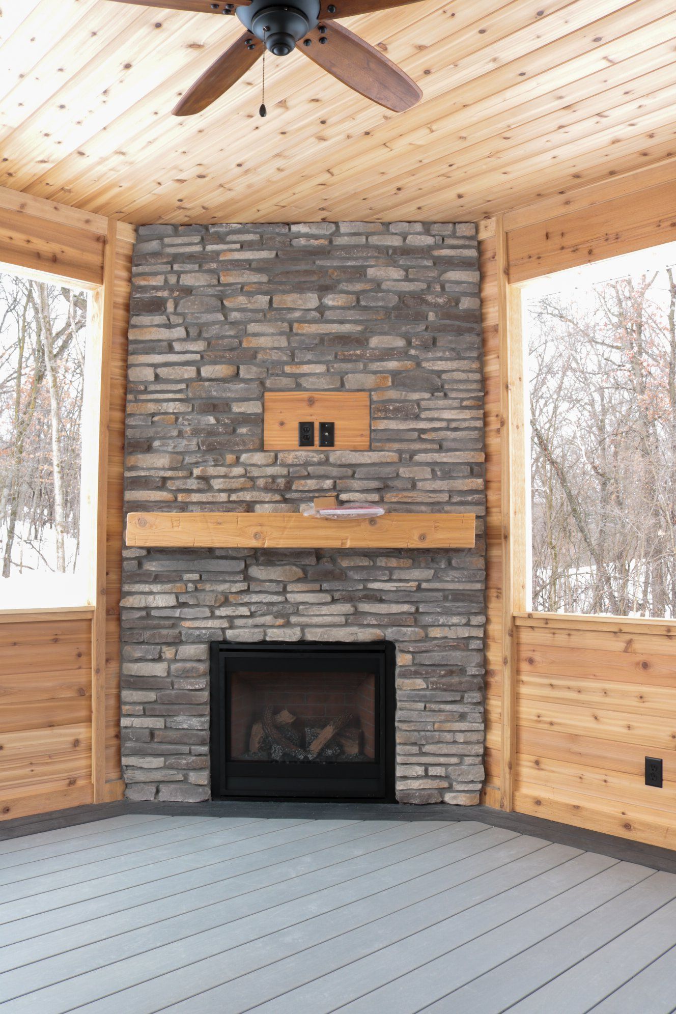 A screened in porch with a stone fireplace and a ceiling fan.