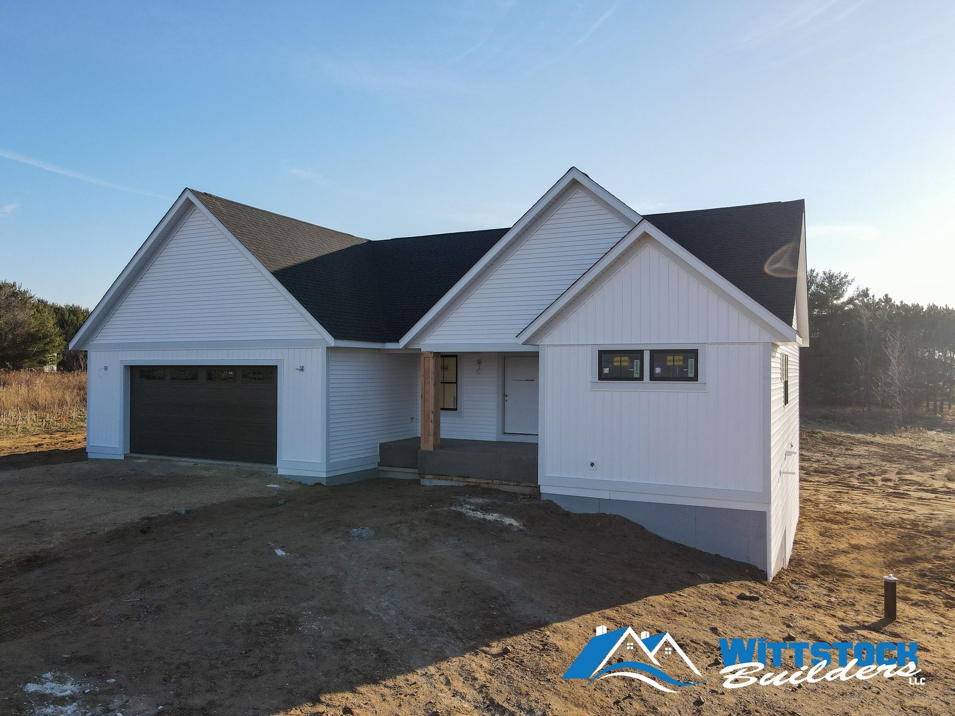 A white house with a black roof is sitting in the middle of a dirt field.