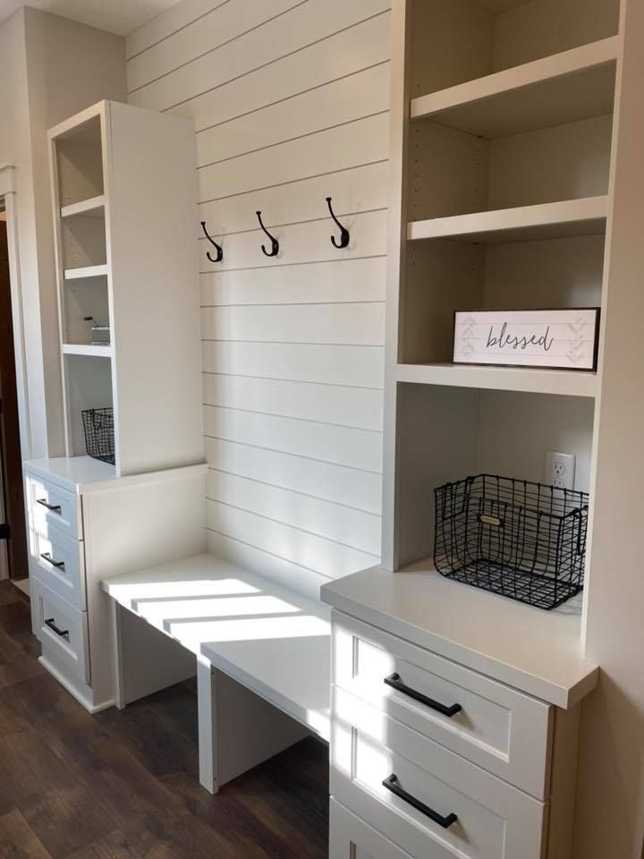 A hallway with a bench, dressers, shelves and hooks.