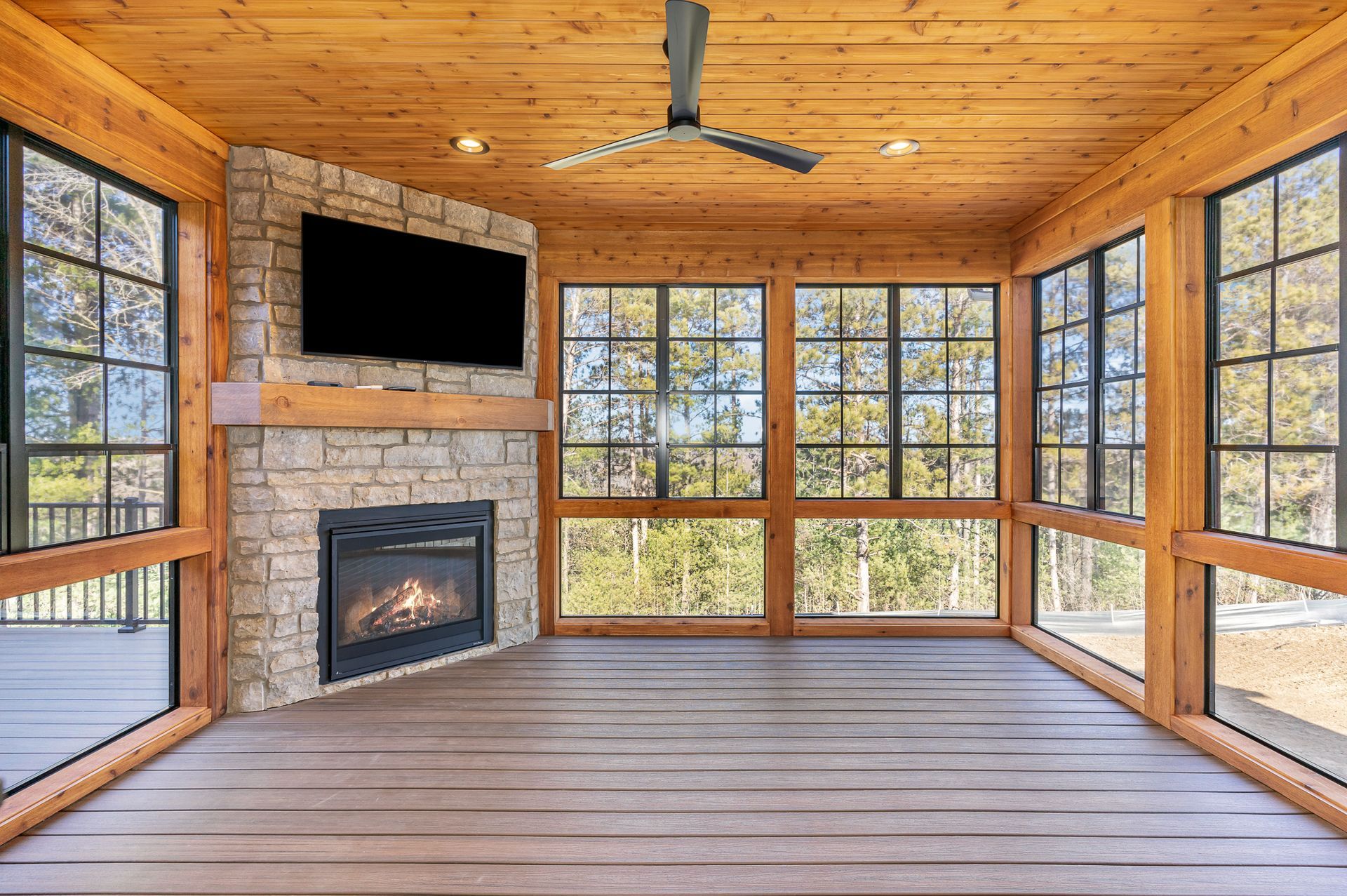 A screened in porch with a fireplace and a flat screen tv.