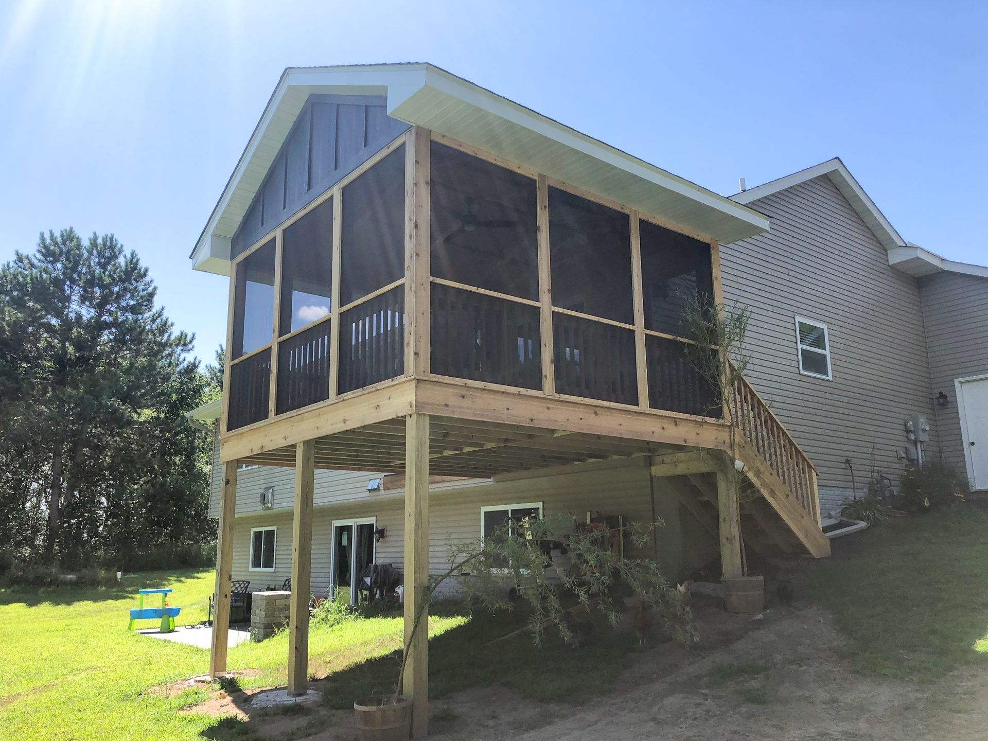 A screened in porch is sitting on top of a wooden deck next to a house.