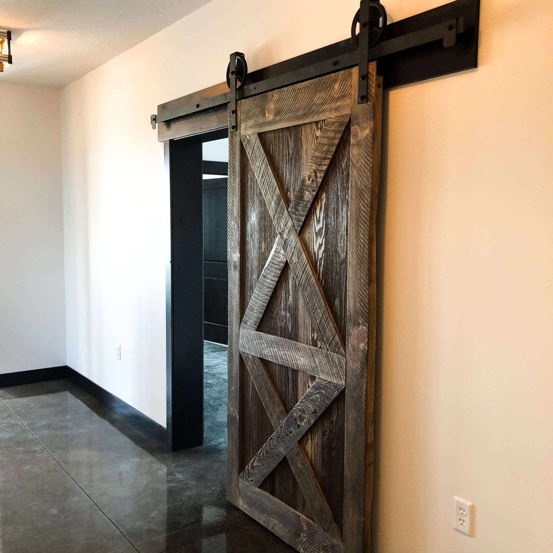 A sliding barn door is hanging on a white wall in a hallway.