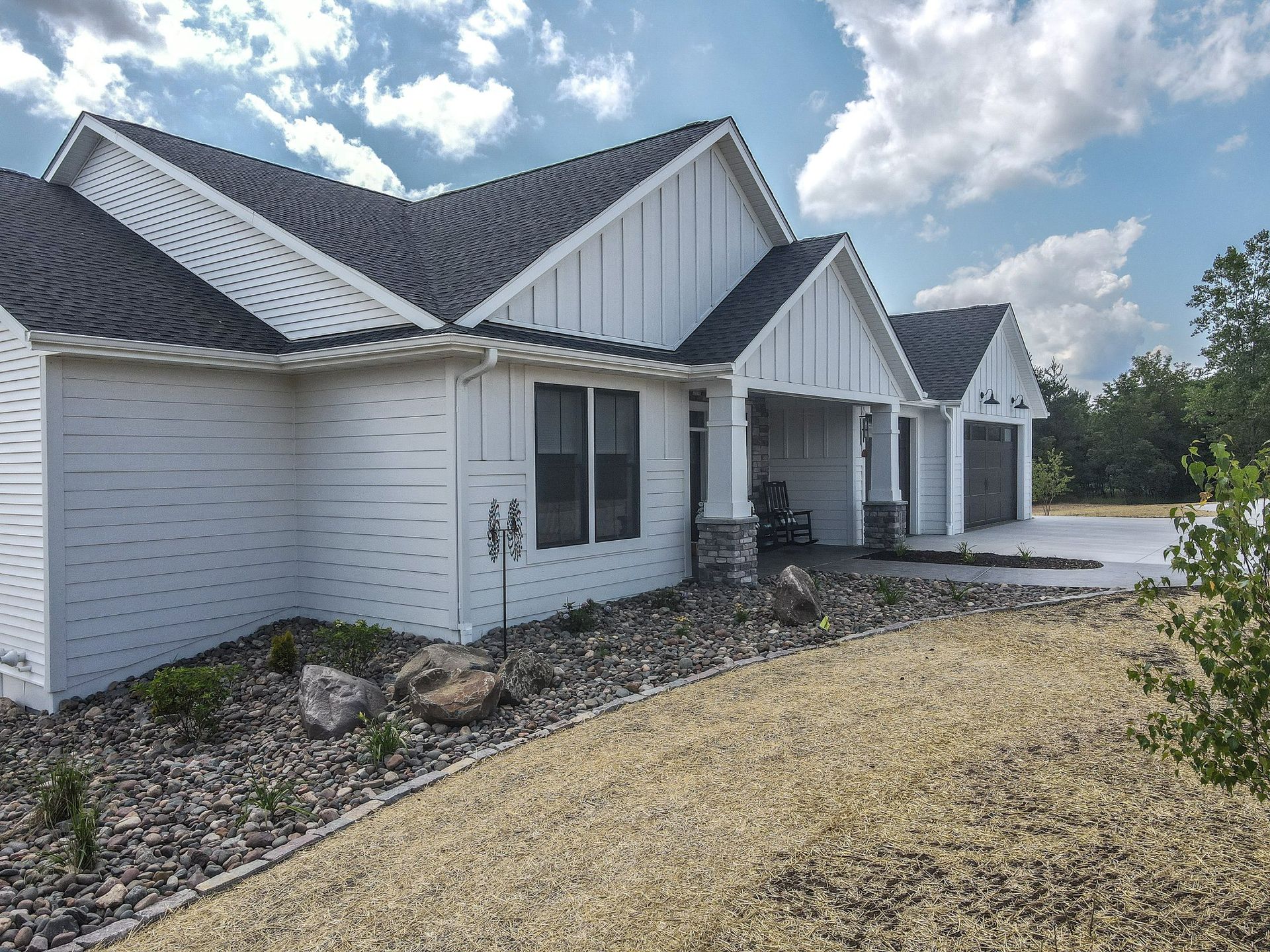 A white house with a black roof is sitting on top of a dirt field.