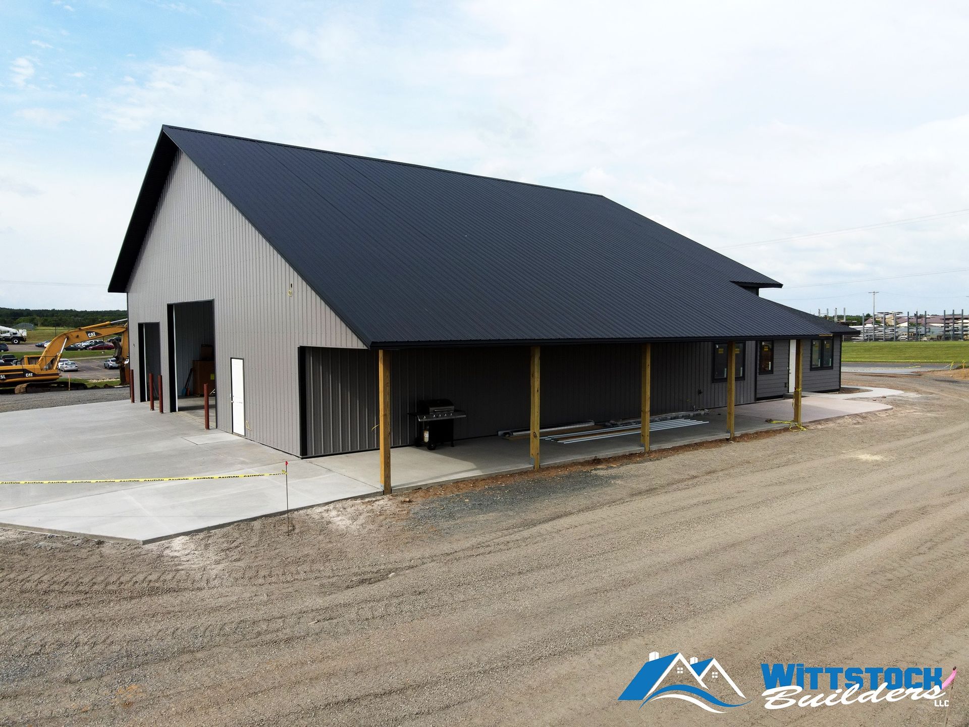 A large barn with a black roof is being built on a dirt road.