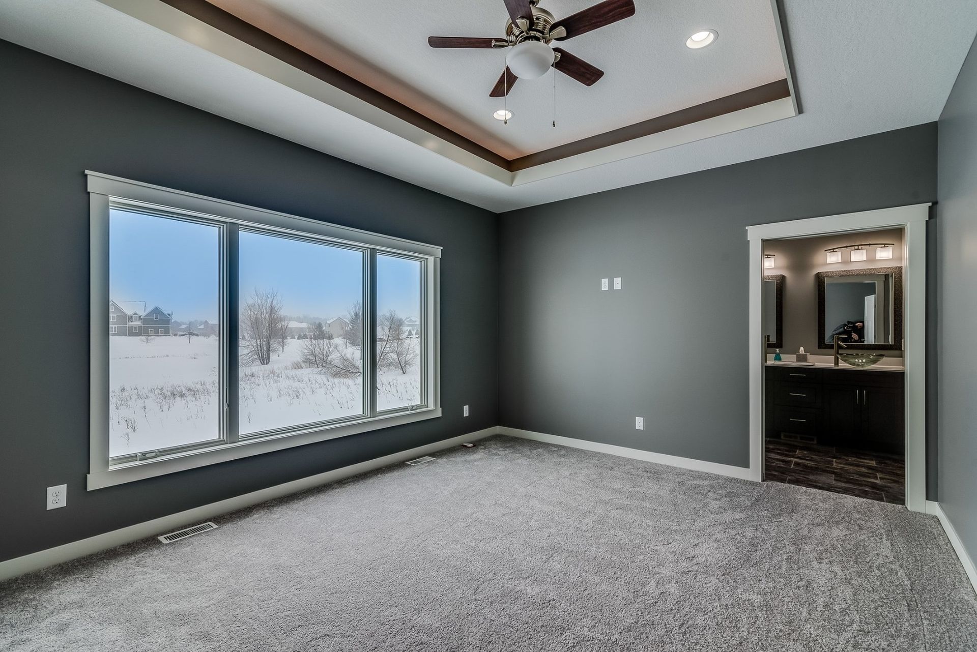 An empty bedroom with a ceiling fan and a large window.