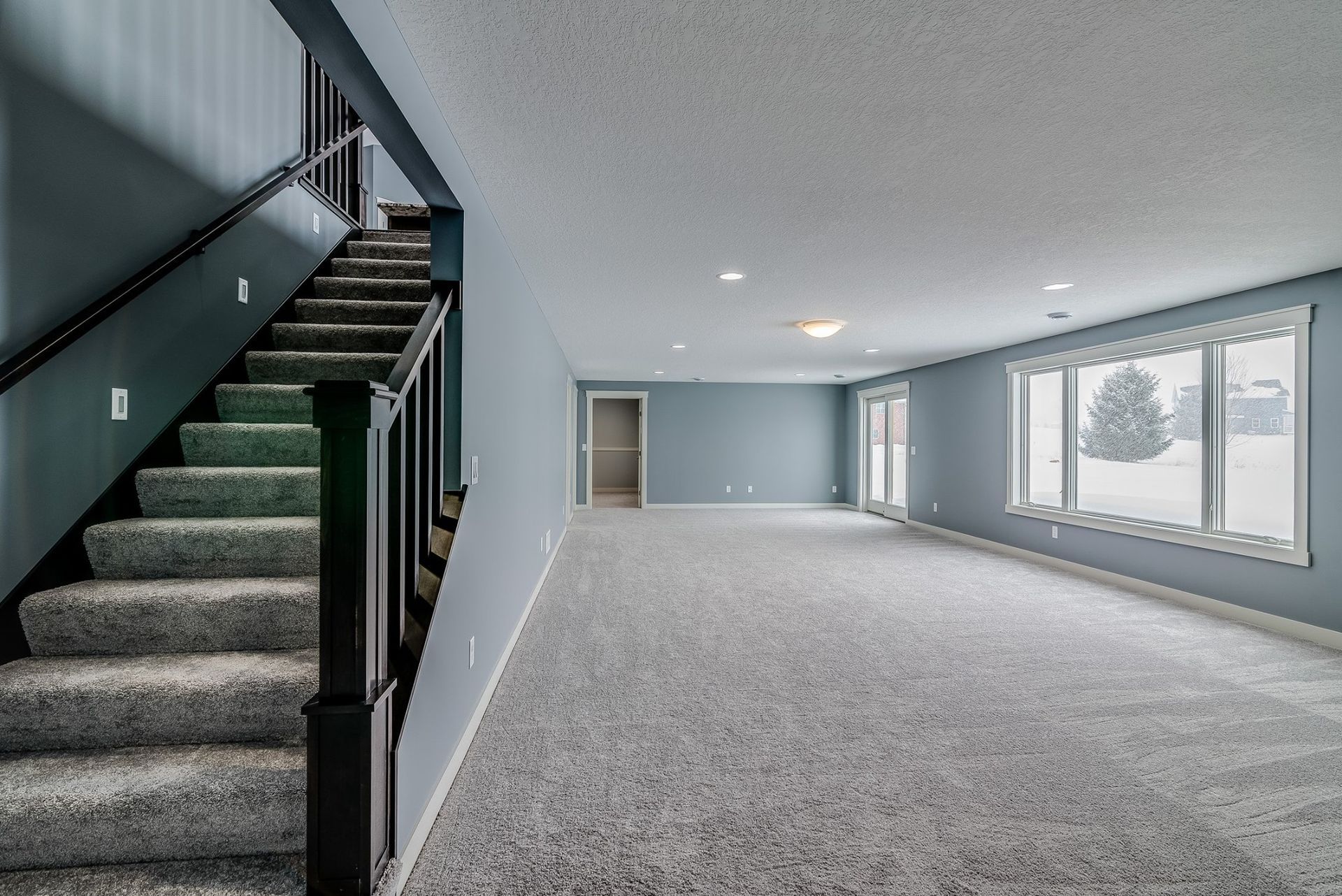 An empty basement with carpeted floors and stairs leading up to the second floor.