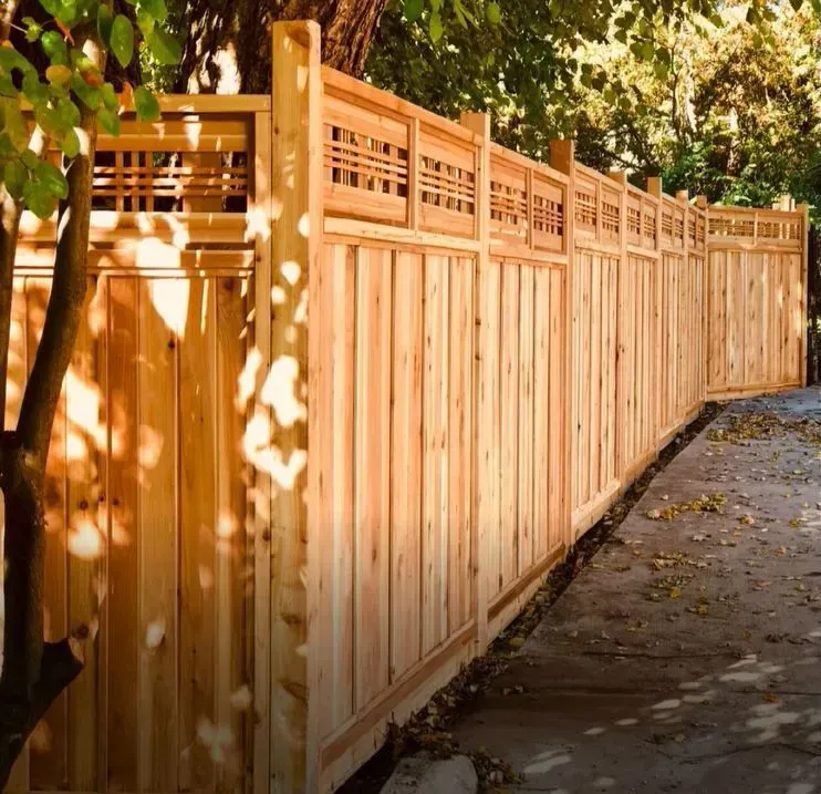 Wooden fence in a yard with decorative top panel and vertical boards.