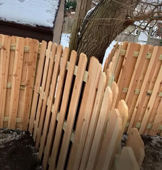 Wooden fence built around a tree trunk in a snowy yard.