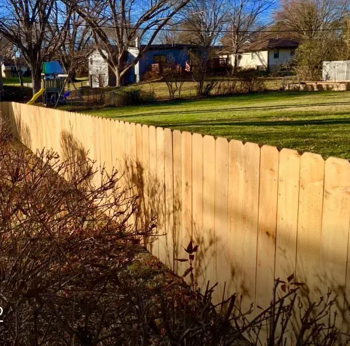 Wooden fence in a sunny backyard, with a playground in the distance.