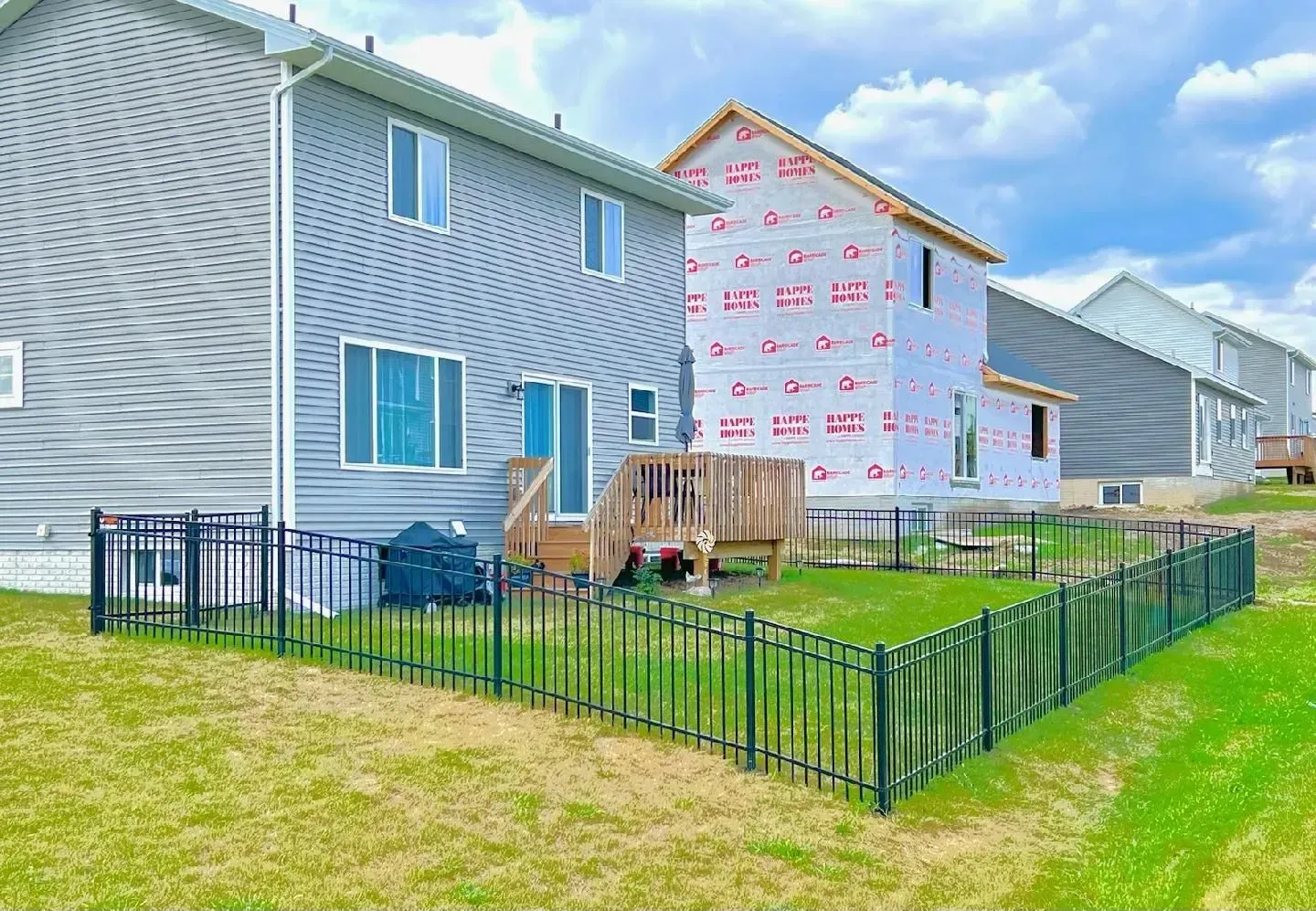 Backyard view of gray houses with a small black fenced yard. One house is under construction.