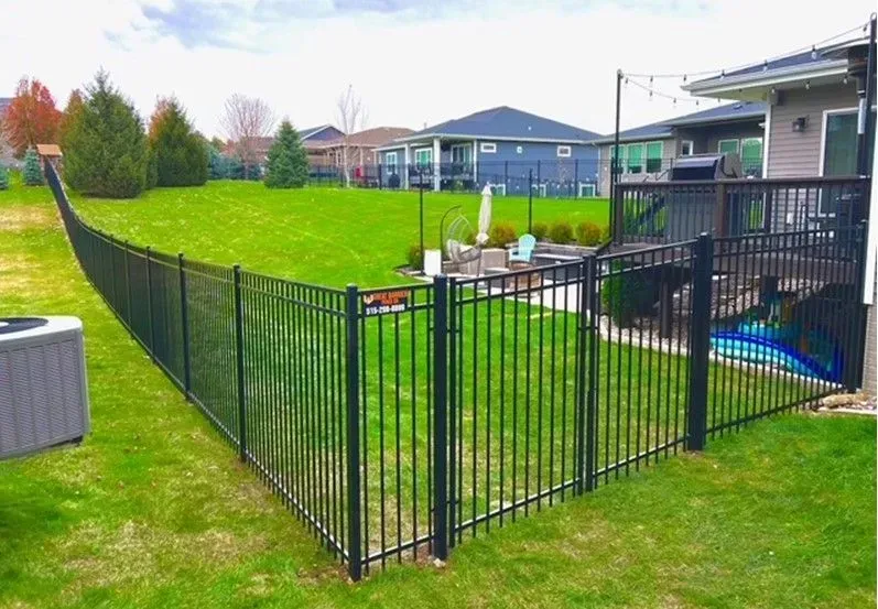 Black metal fence encloses a green backyard, separating a deck with a house in the background.