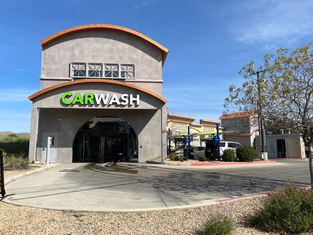 A beige car wash building with an arched entrance under a bright blue sky, surrounded by desert landscaping.