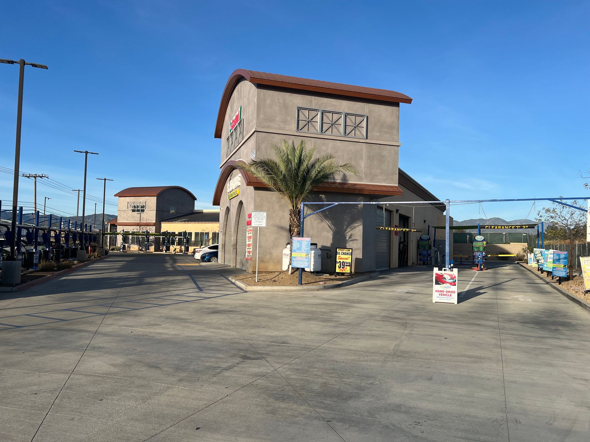A drive-through car wash facility with a tan stucco building under a clear blue sky on a sunny day.