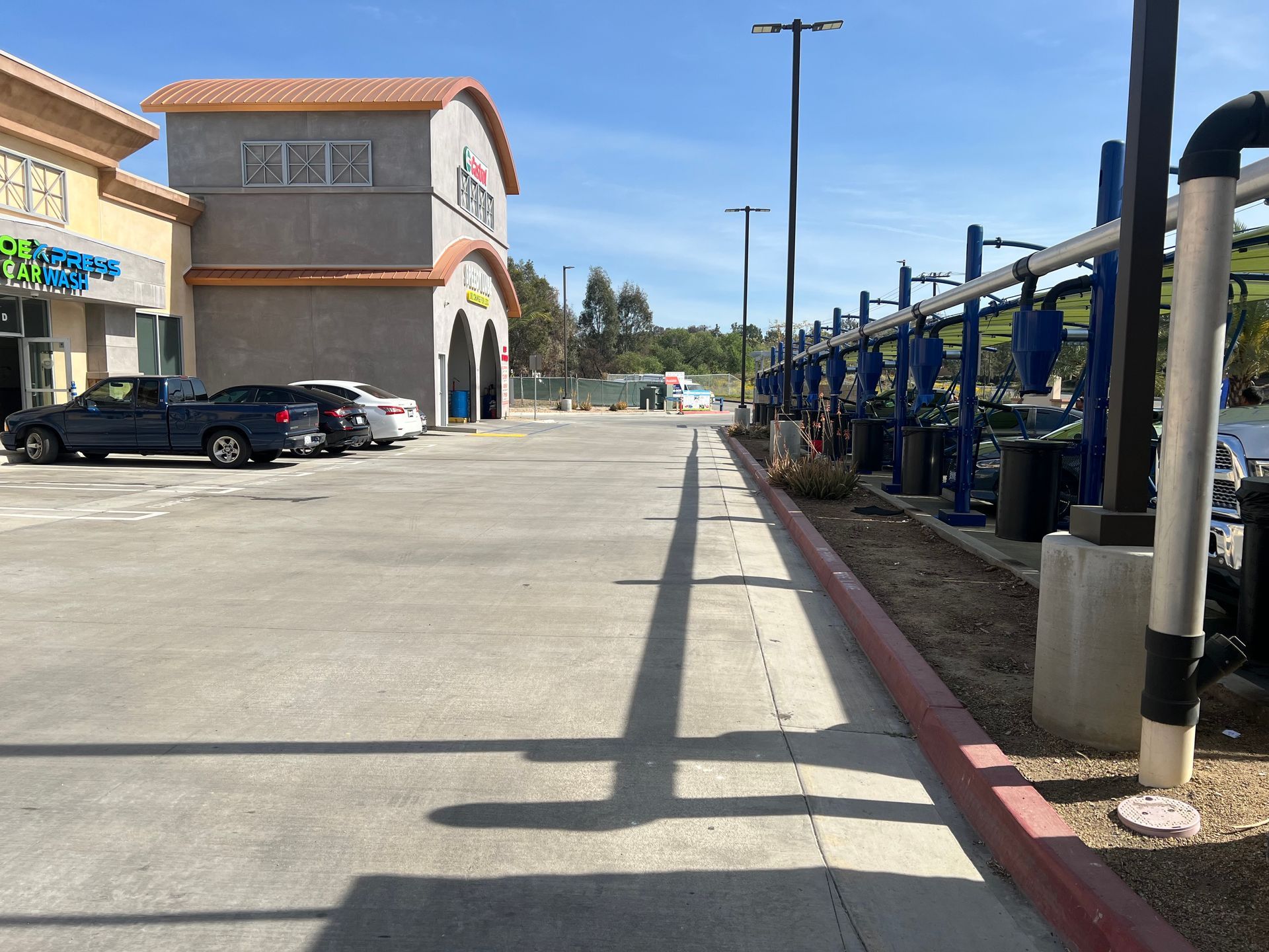 A paved parking lot with a car wash structure on the right and a beige building with arched entries on the left.