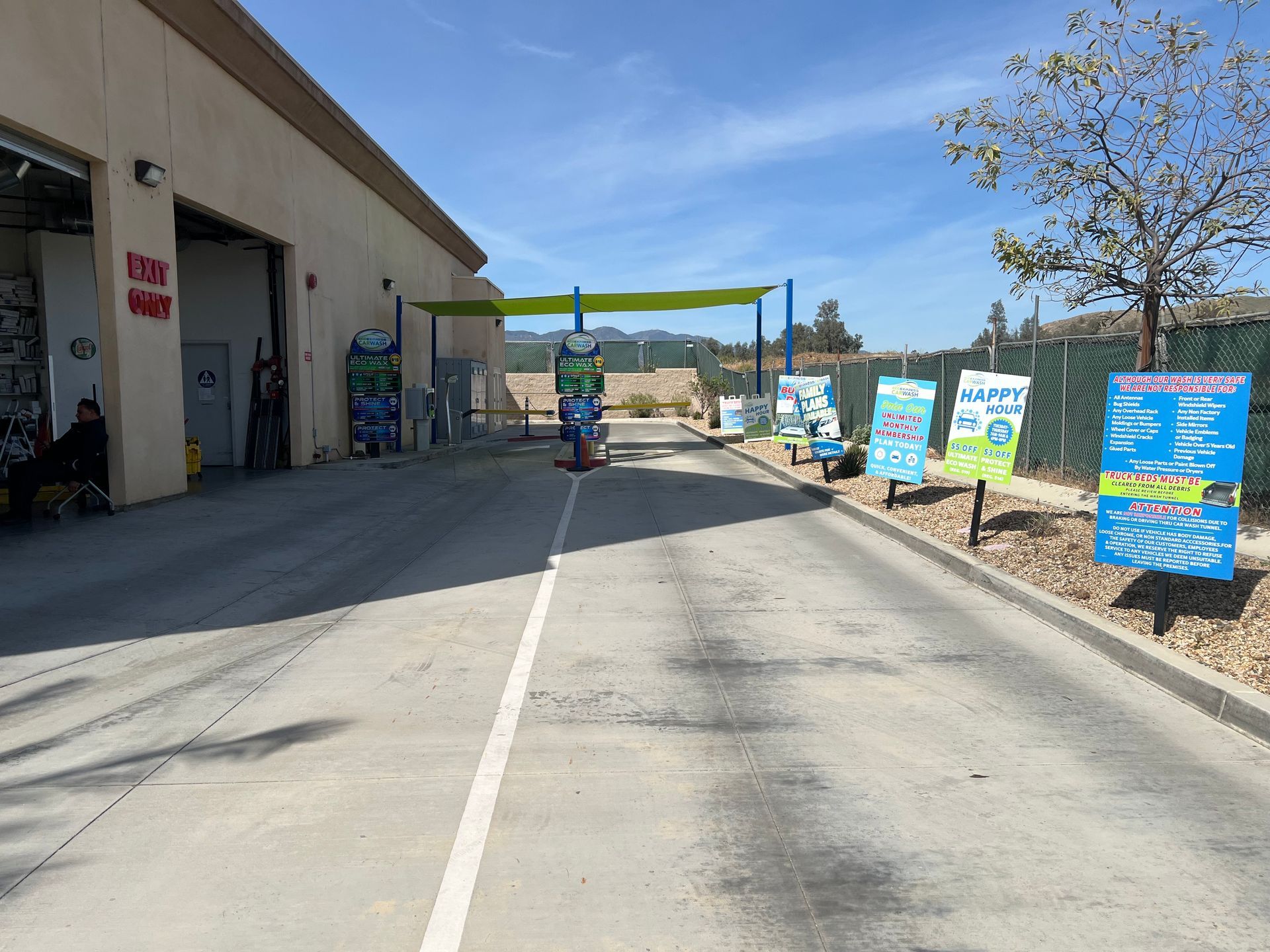 The entrance to a car wash facility with a concrete driveway, signage, and a lime green overhead shade canopy.
