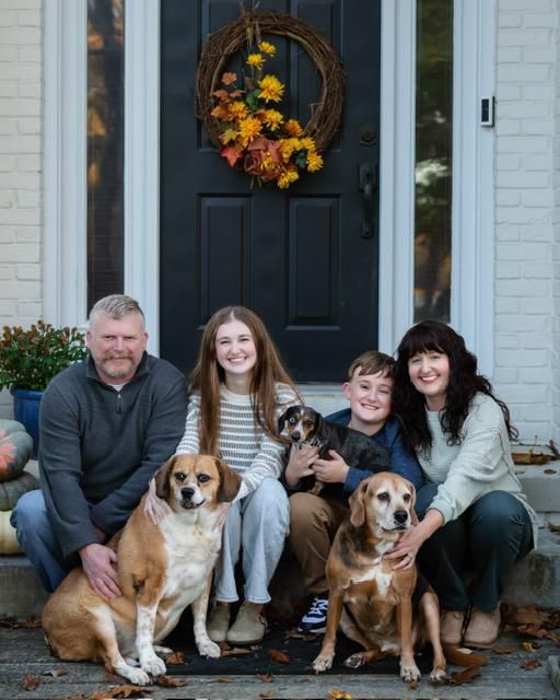 Family and three dogs on front steps; fall wreath on door.