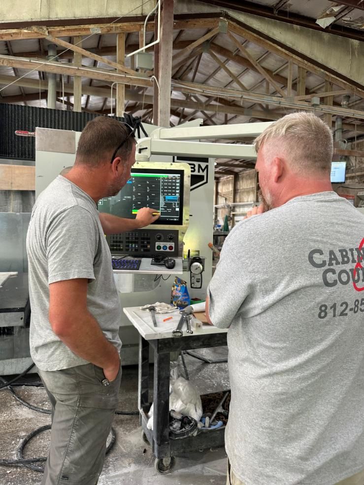 Two men operating machinery, one points to a screen, the other watches. In a factory setting.