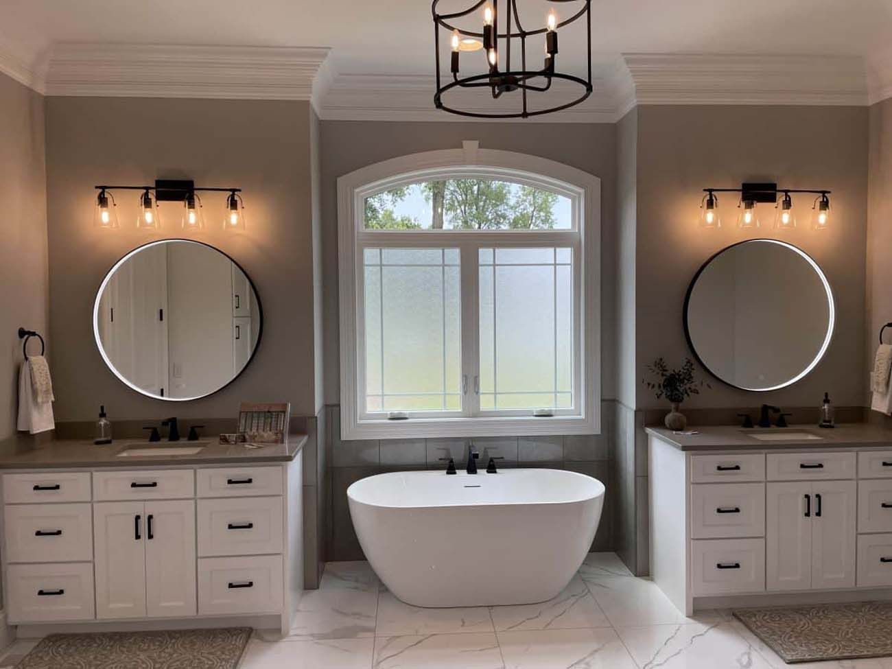 Bathroom with white cabinets, round mirrors, and a freestanding tub. Neutral color scheme with modern light fixtures.