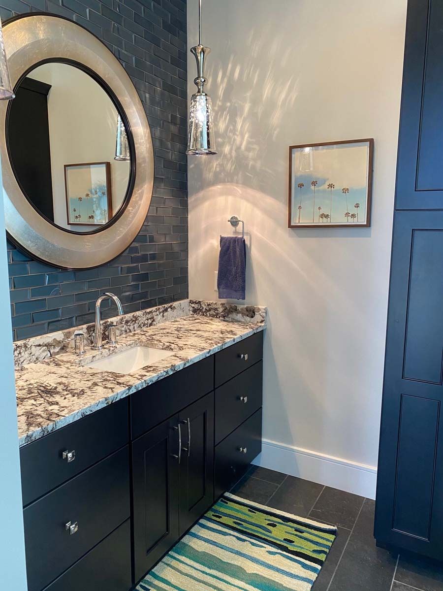 Powder room with dark cabinetry, patterned countertop, and a circular mirror.